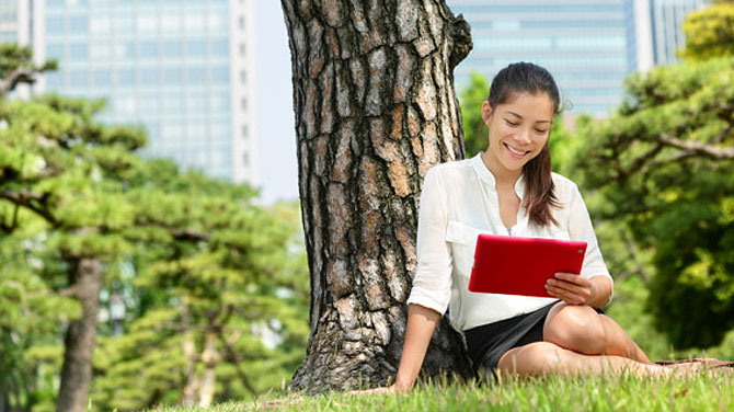 Lady sat on grass by a tree holding a tablet computer