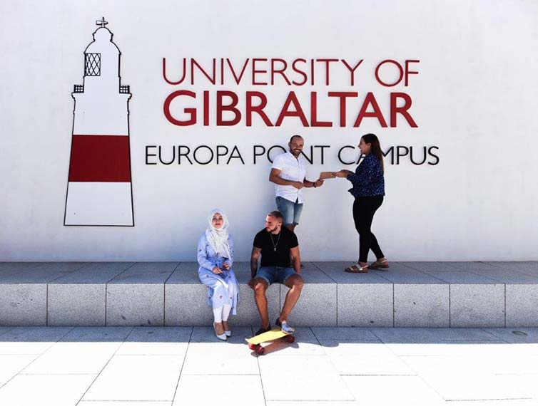 Four students sat by University mural