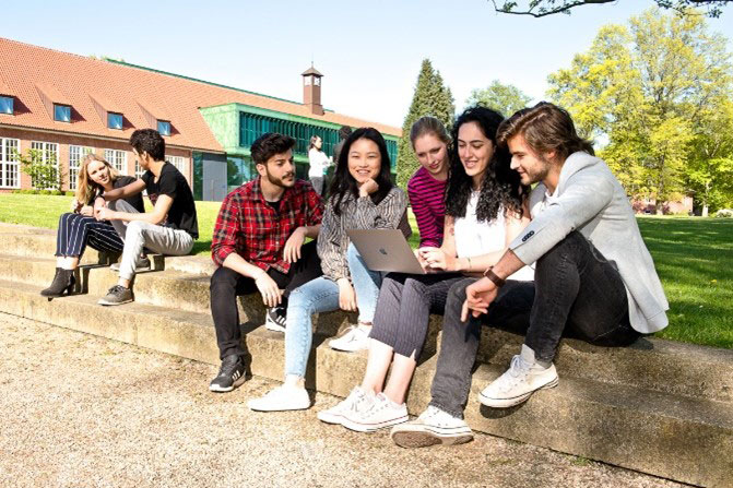 Smiling group of students outside on campus looking at a laptop
