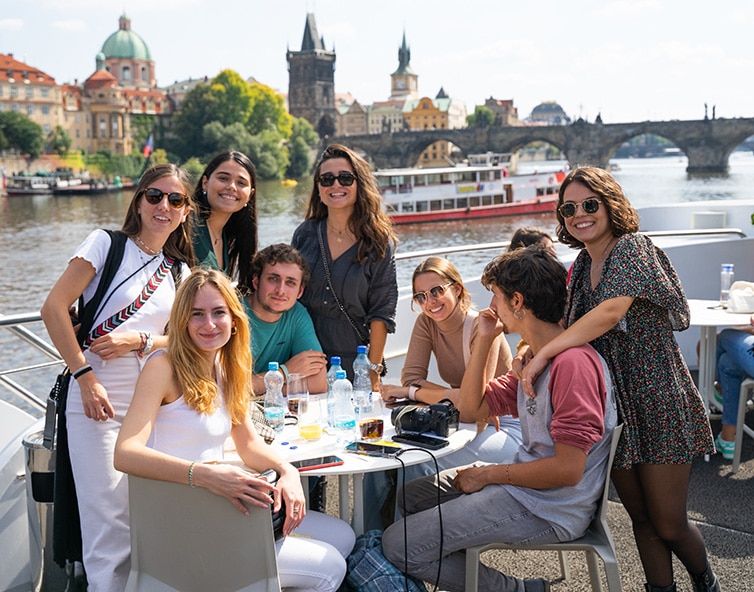 Students sat on sunny patio with river in background