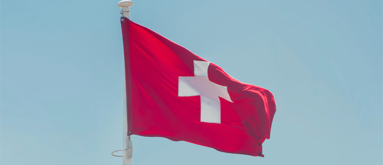 Image of the Swiss flag flying on a flagpole with a bright blue background