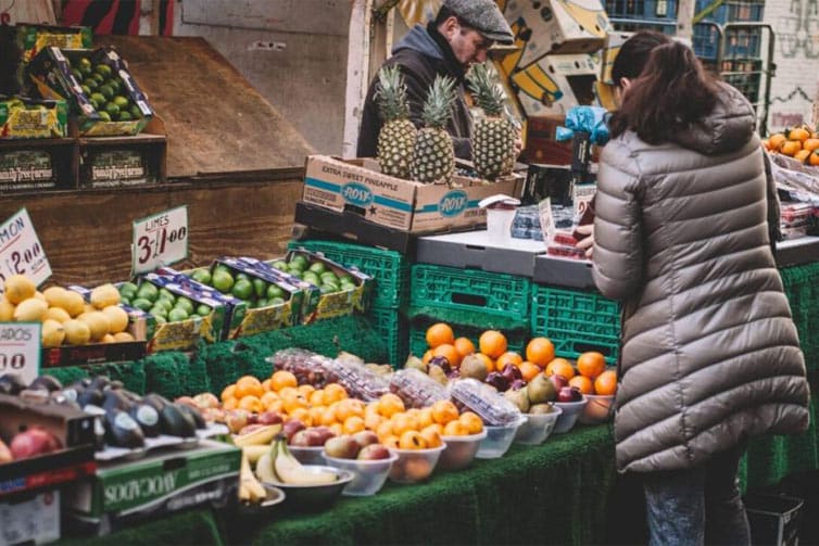 Image of a person wearing a jacket looking at a market stall of colourful fruit
