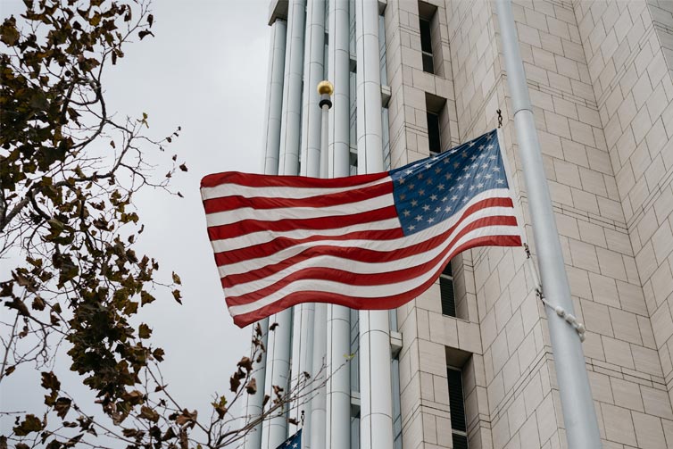 Image of the US flag flying on a flagpole in front of a building