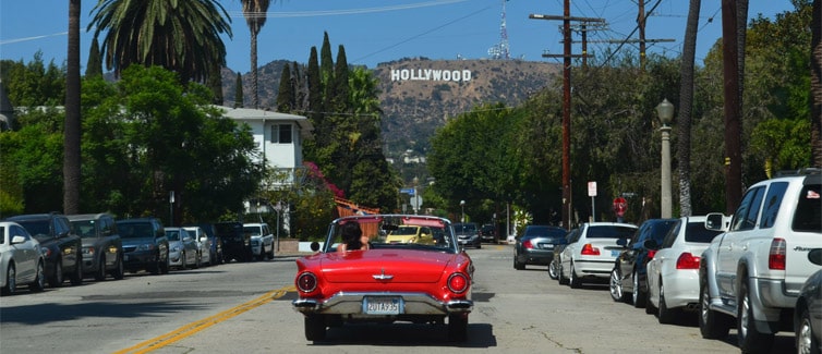 A bright red vintage car driving along a road in the direction of the Hollywood sign