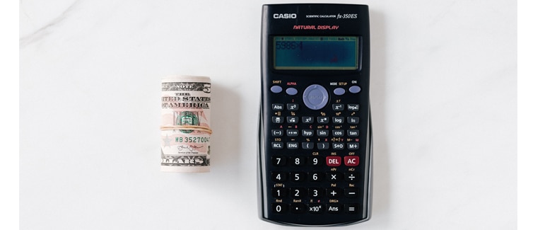 Roll of US Dollar notes next to a calculator placed on a white background