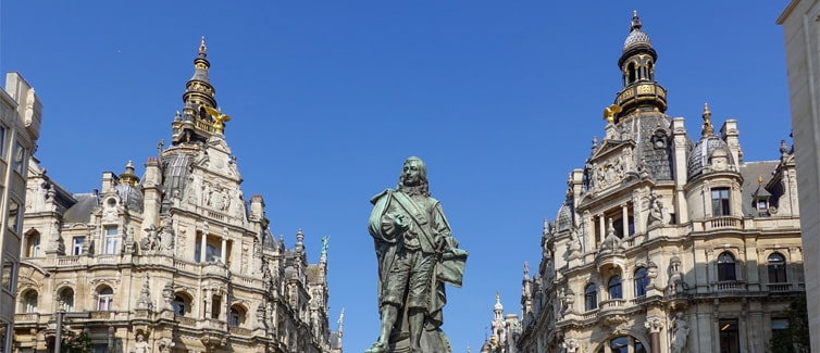 Image of two buildings with a blue sky in the background and a statue of a man in the foreground