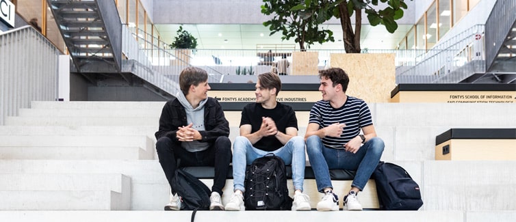 Image of three students sitting on a step and smiling at each other