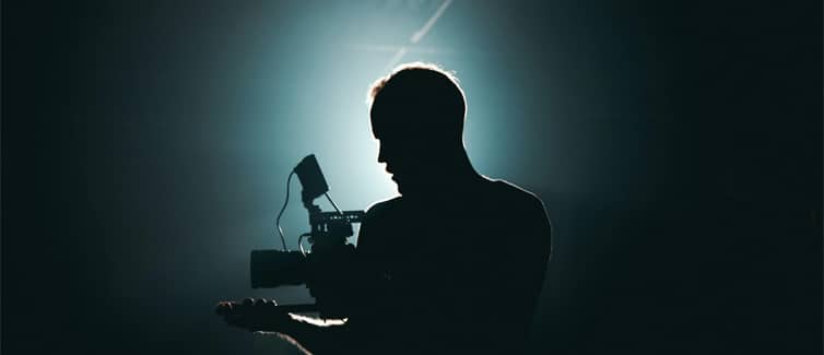 Image of a person holding a camera in a dark room with a bright white light shining from behind his head