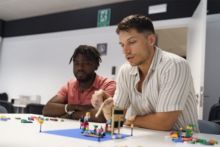 2 students sat at a table and looking at lego pieces