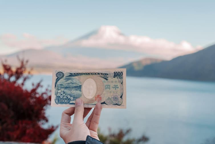 Image of a hand holding a 1,000 Yen note with a mountain in the background.