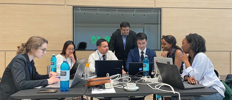 A group of students sat around a table looking at their laptops and each other