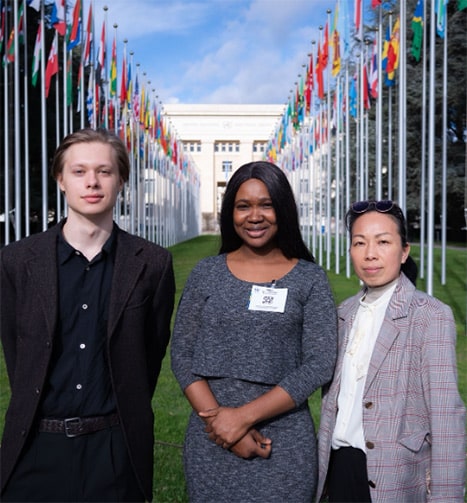 Three students stood outside of a big white building with rows of flags behind them