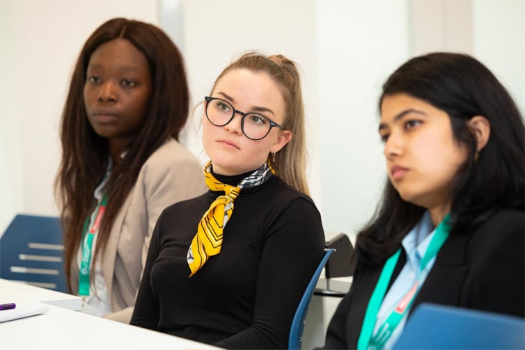 Three students sat at a desk looking away from the camera