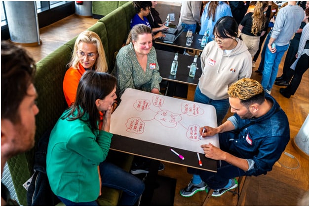 Several students sat around a table looking at a large sheet of paper that has red writing on it