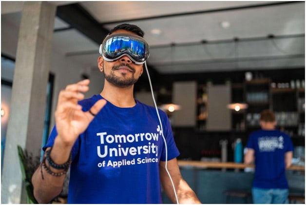 A student wearing a virtual reality headset and a purple t-shirt with the text 'Tomorrow University of Applied Sciences' printed on it