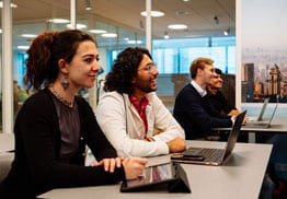 Four students sitting at desks with laptops in front of them