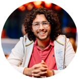 Image of a male student with curly brown hair and glasses smiling towards the camera