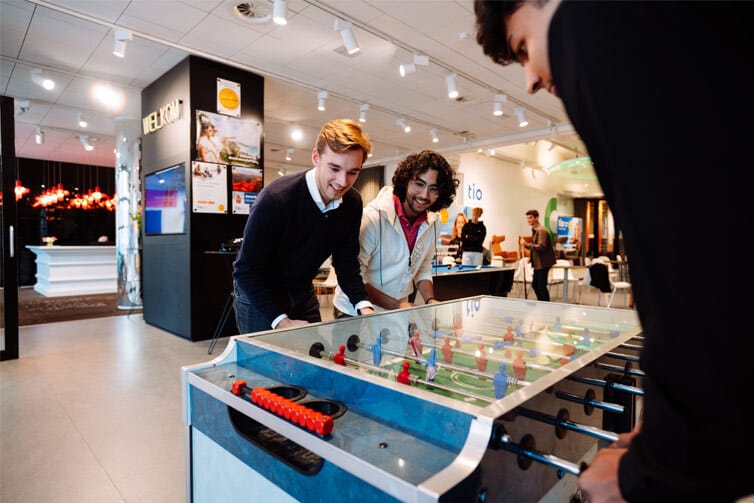 Three students playing table football together in a large games room